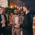 Three well-dressed men drinking whiskey and communicating while spending time on party